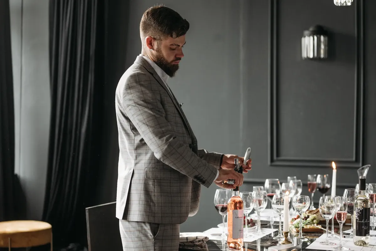 A sommelier opening wine bottles for a formal wine tasting setup indoors.