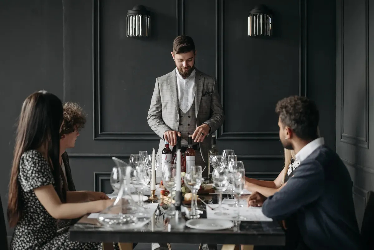A sophisticated indoor dining setup with a sommelier presenting wine to seated guests.