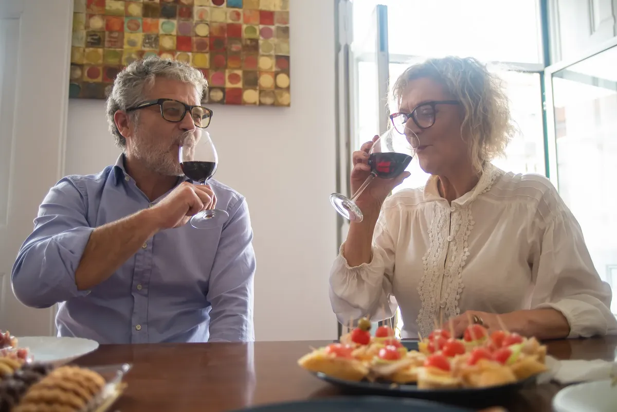 Senior couple enjoying wine and snacks at home, showcasing joyful companionship and relaxed dining.