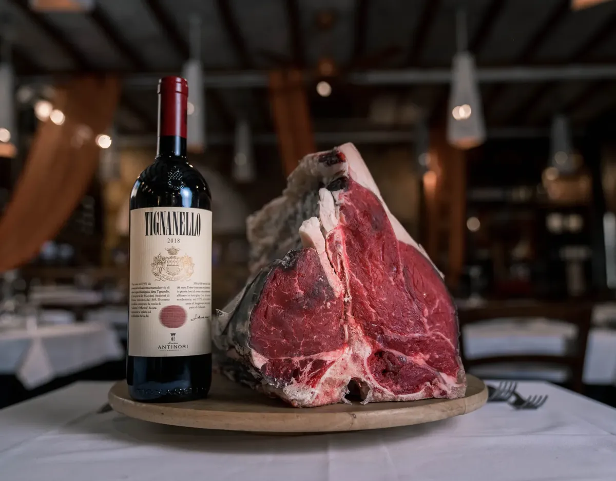 A luxurious pairing of raw steak with a bottle of premium red wine on a restaurant table.