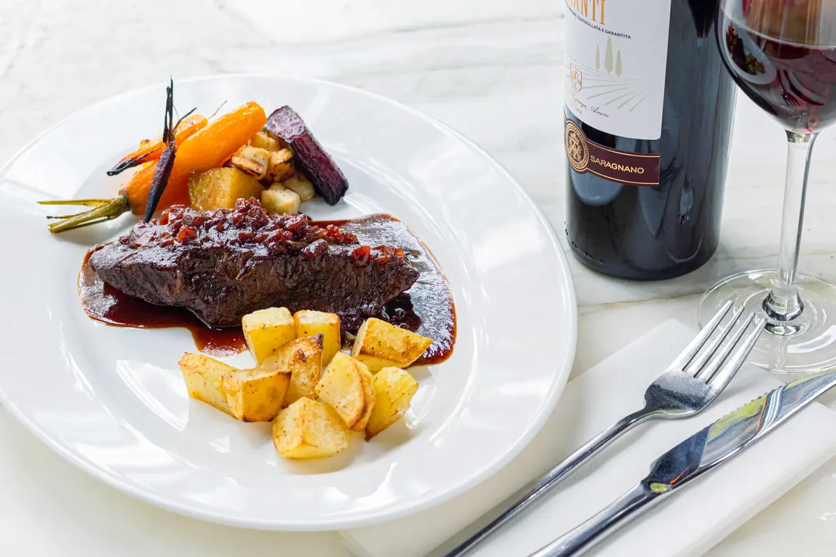 Elegant gourmet meat dish served with vegetables and a glass of red wine.