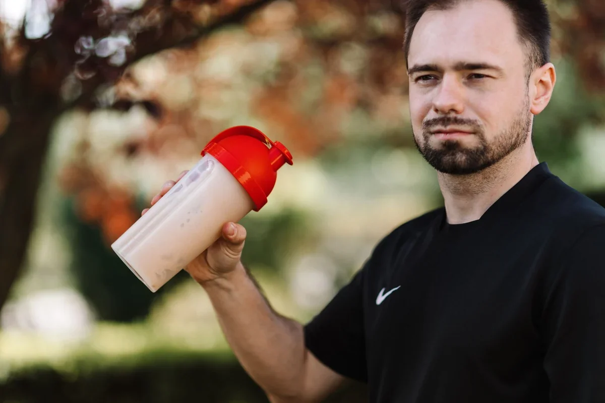 Une main tenant un shaker de protéines en plastique avec une paille