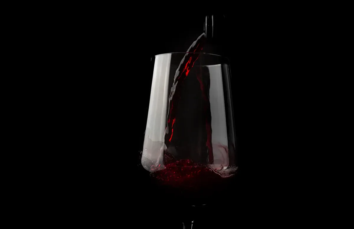 Elegant and dramatic close-up of red wine being poured into a glass against a black background.